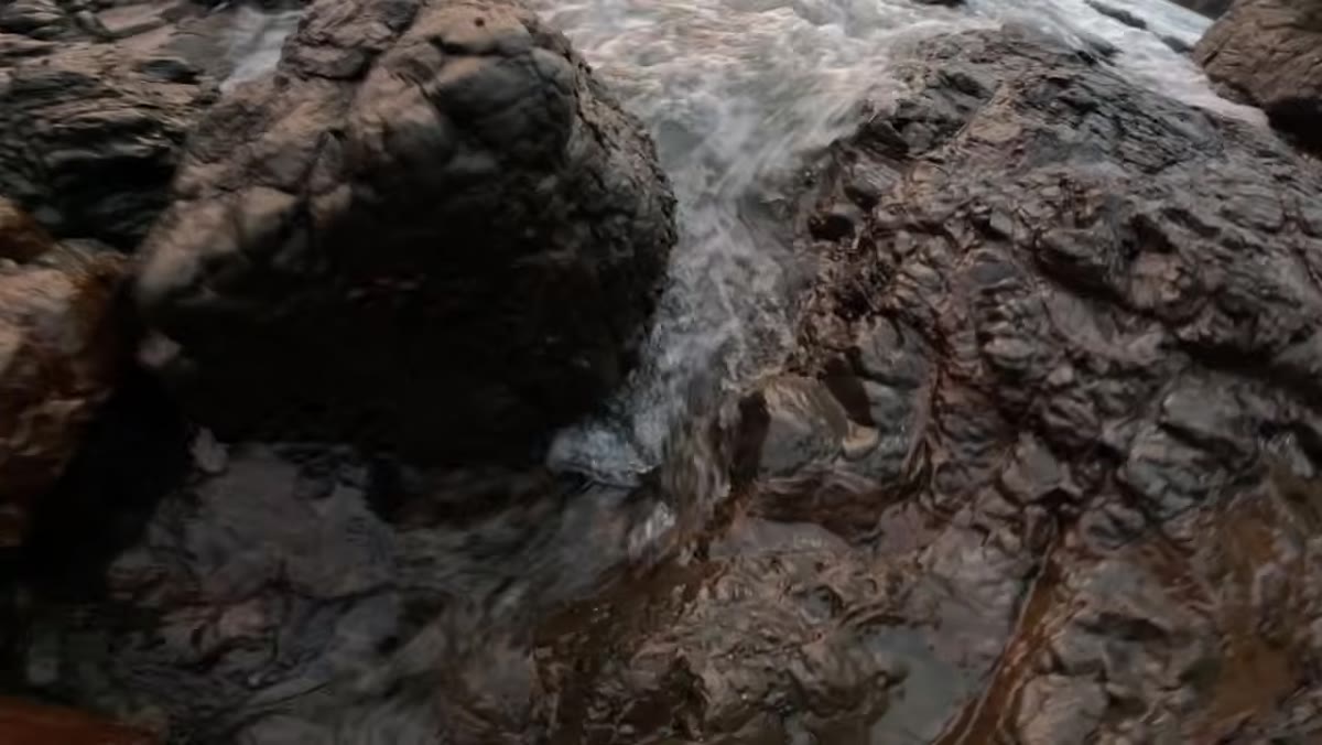 Patino crouching low, identifying a gap between rocks where water flows