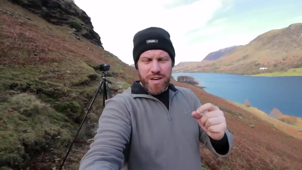Hiker on lower slopes with wide valley views opening behind him