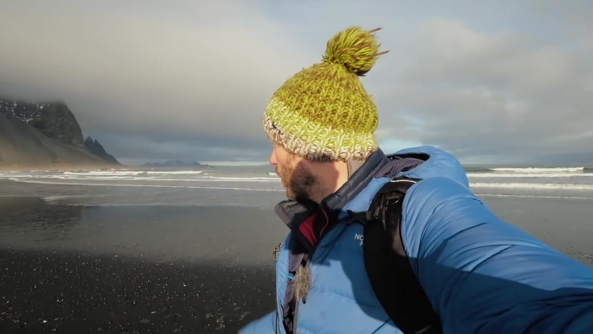 Danson at black sand beach with mountains and ocean behind him